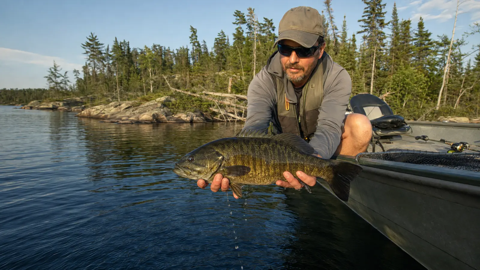 An angler holds a large smallmouth bass beside a boat on a remote Gowganda-area lake.